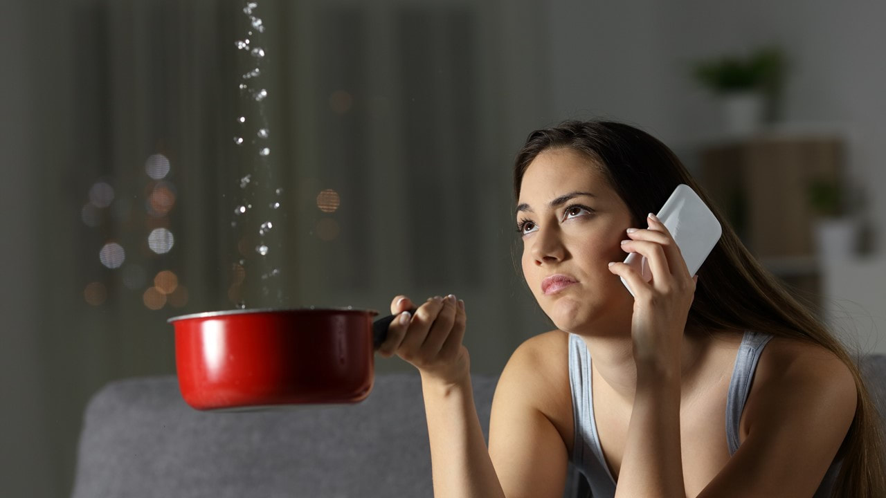 Image of a woman holding a red pot catching water leaking from the ceiling - renters insurance - lake charles la - kelly lee insurance